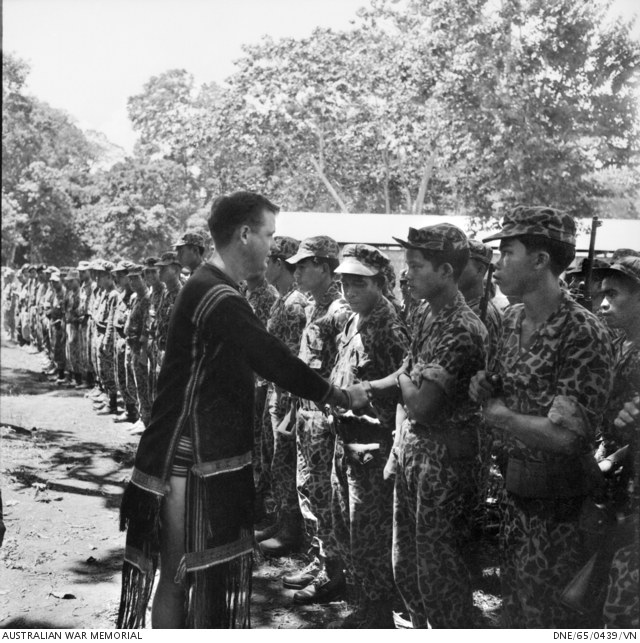 An Australian officer in highland dress shakes hands with a line of highland soldiers in camouflage uniforms