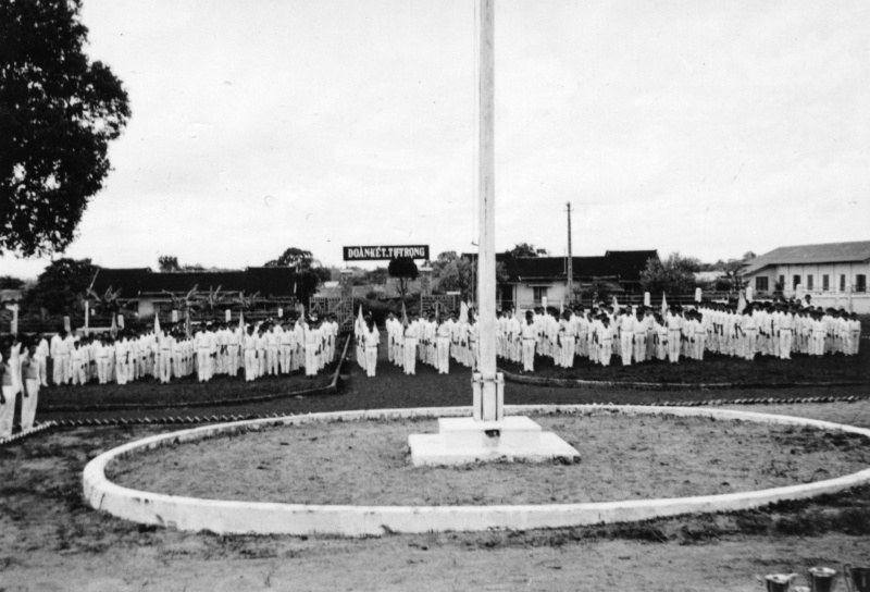 Rows of students in white shirts standing around a flagpole in a school yard