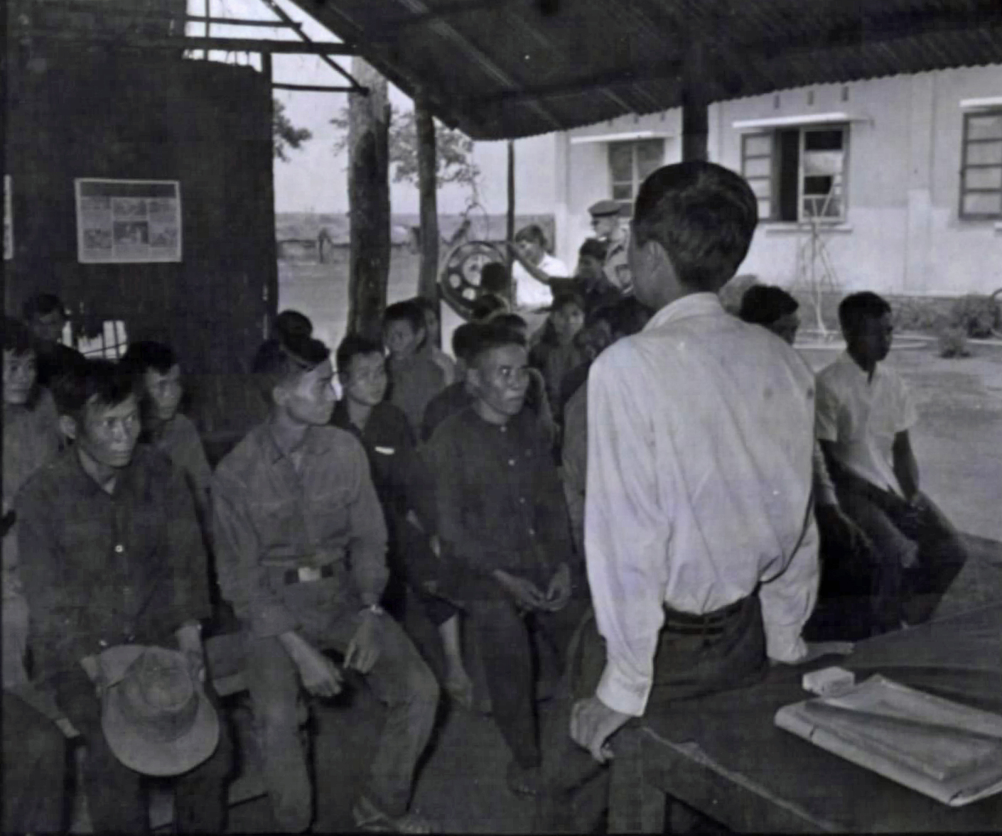 A man standing before a blackboard lecturing a seated class