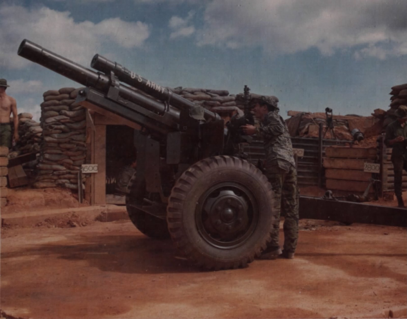 A soldier sighting a howitzer inside a sandbagged position