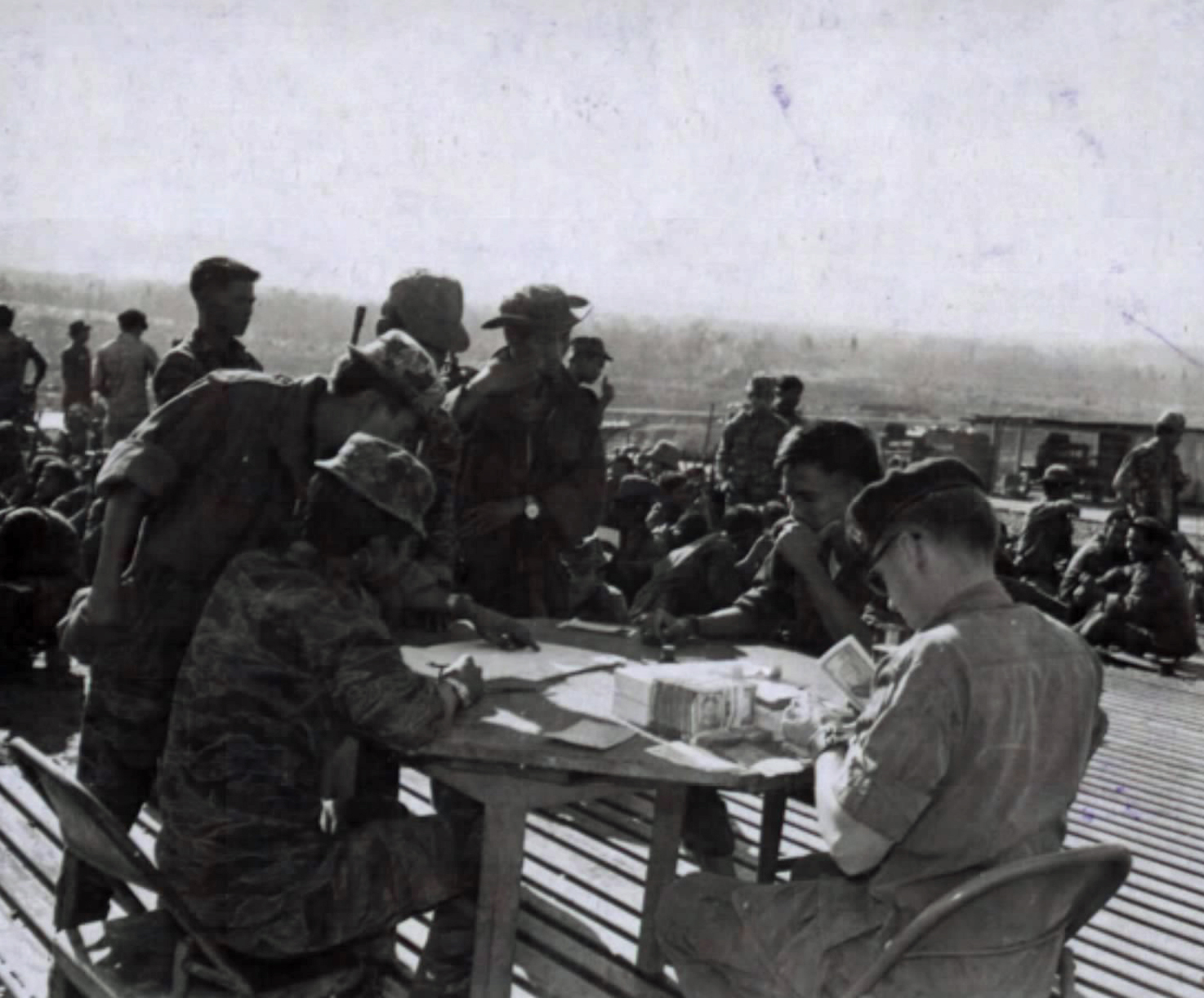 An American officer at a table counting money while soldiers wait in line