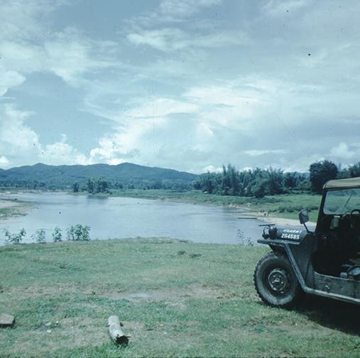 A wide river running between low hills, with an American army jeep parked on the grass in the foreground