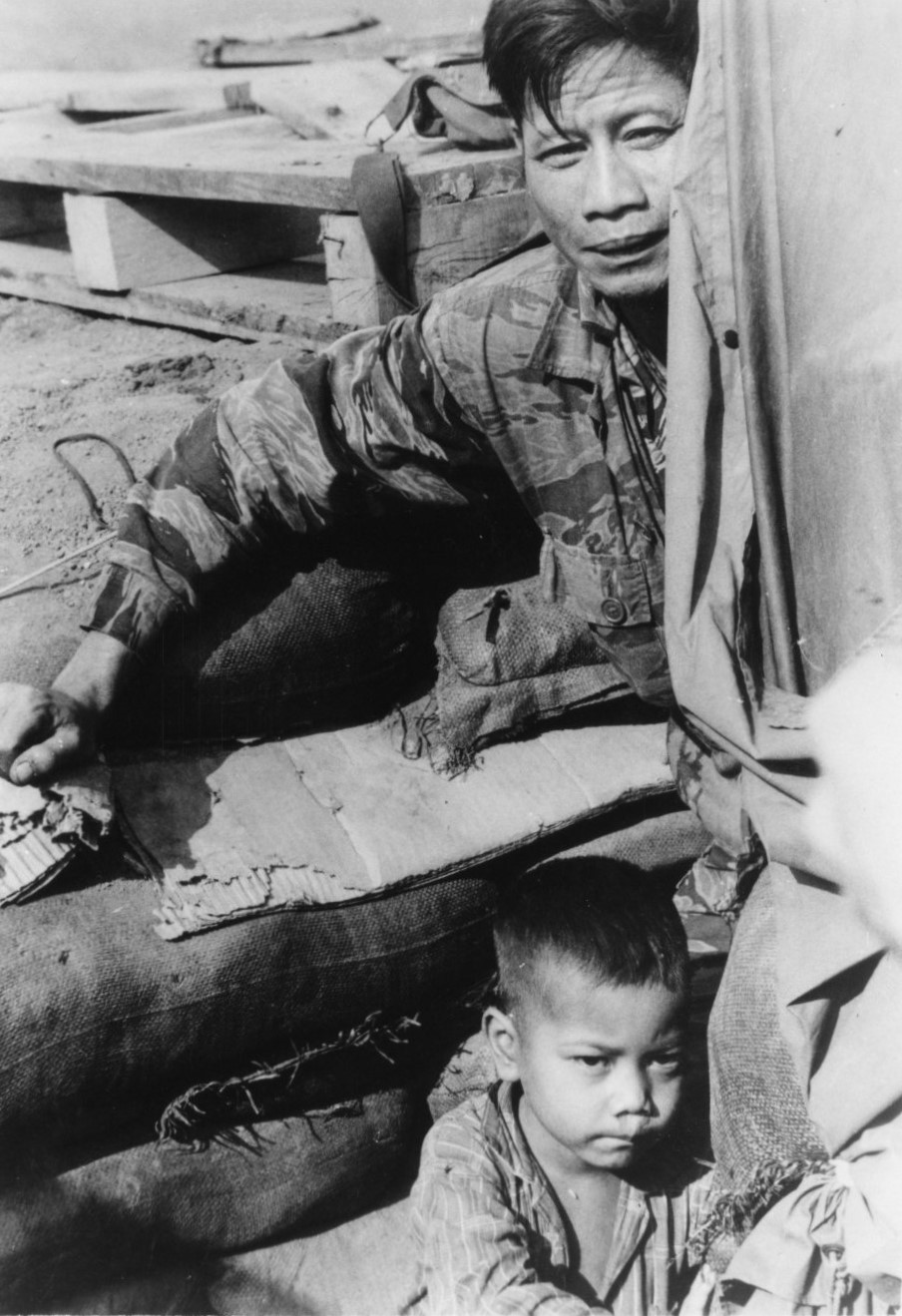 A soldier sitting with a small boy among sandbags