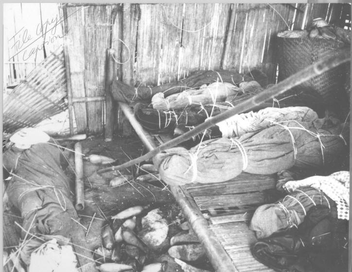 Bodies wrapped in cloth and mats, tied with cord, inside a damaged bamboo house