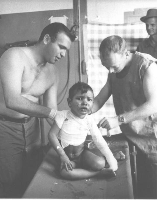 Two American medics treating a small bandaged boy seated on a table
