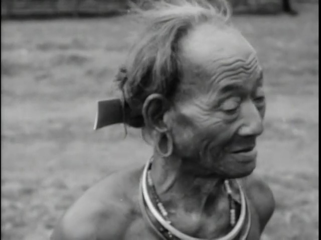An elderly highland man with large ear plugs and necklaces of beads, smiling
