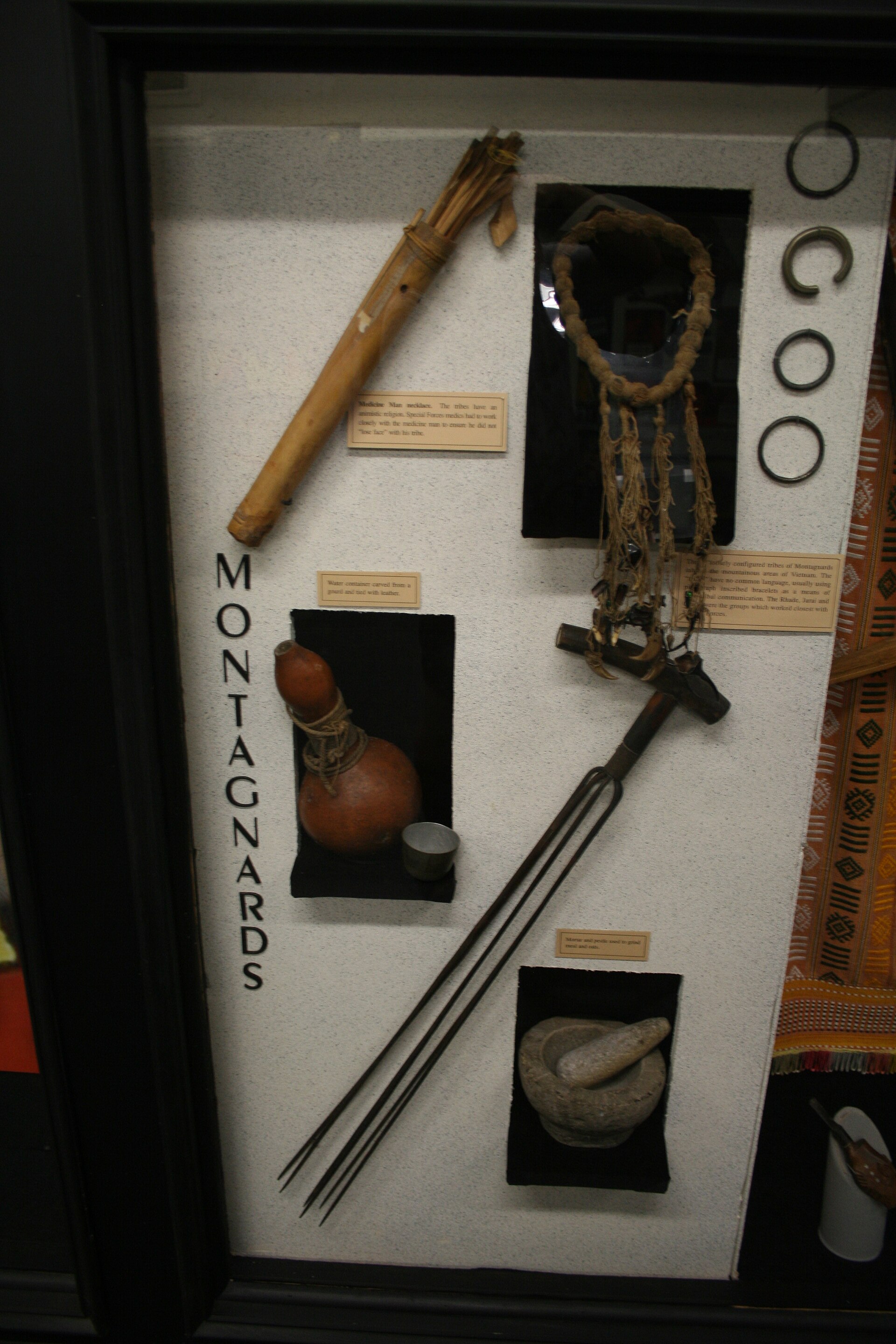 A museum display case with a Montagnard crossbow, a bracelet, a knife and other objects