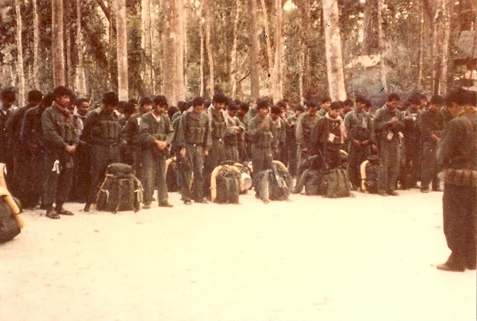 Rows of men in uniform with packs standing in a forest clearing