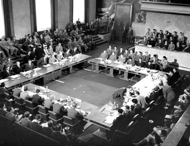 Delegates seated around a large square of tables in a conference hall at Geneva in 1954