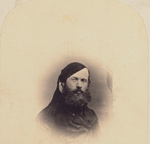 A small photograph of a bearded man in a dark coat, mounted on a card