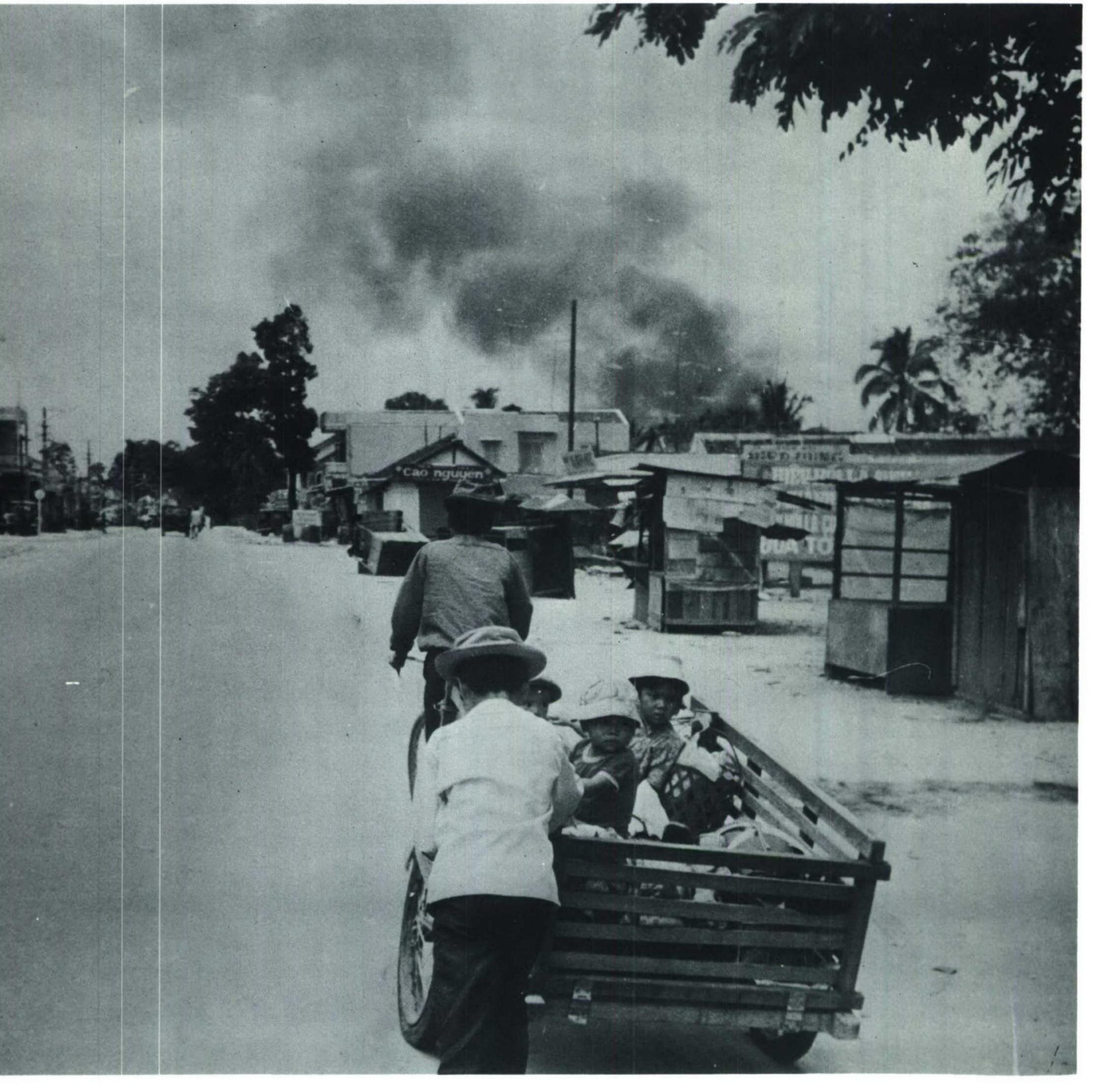 Refugees on a cart on a road with smoke rising over a town