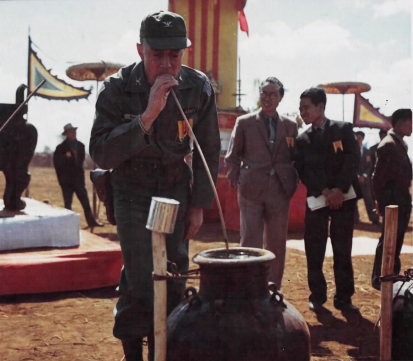 An American officer drinking through a long straw from a large jar at a ceremony