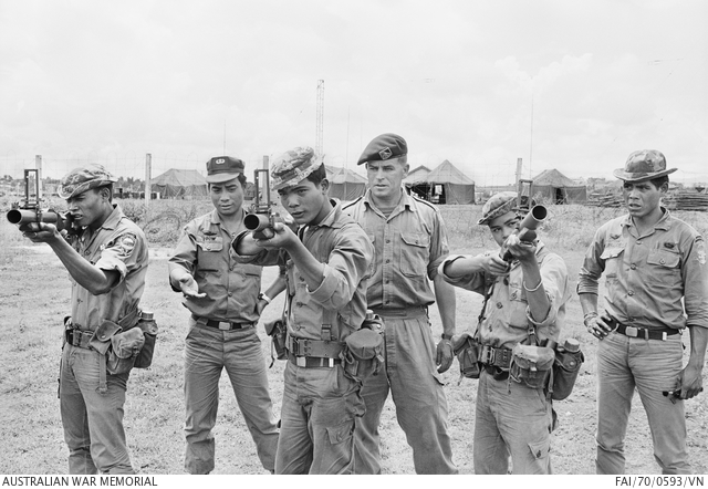Two officers show a group of highland soldiers how to fire a grenade launcher