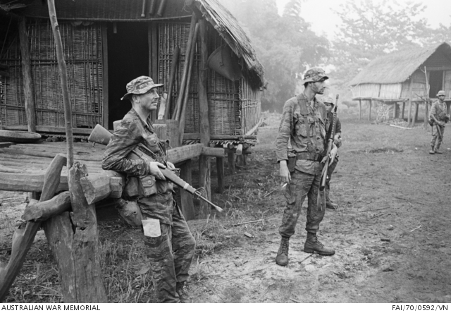 Soldiers moving through a highland village while two advisers look on