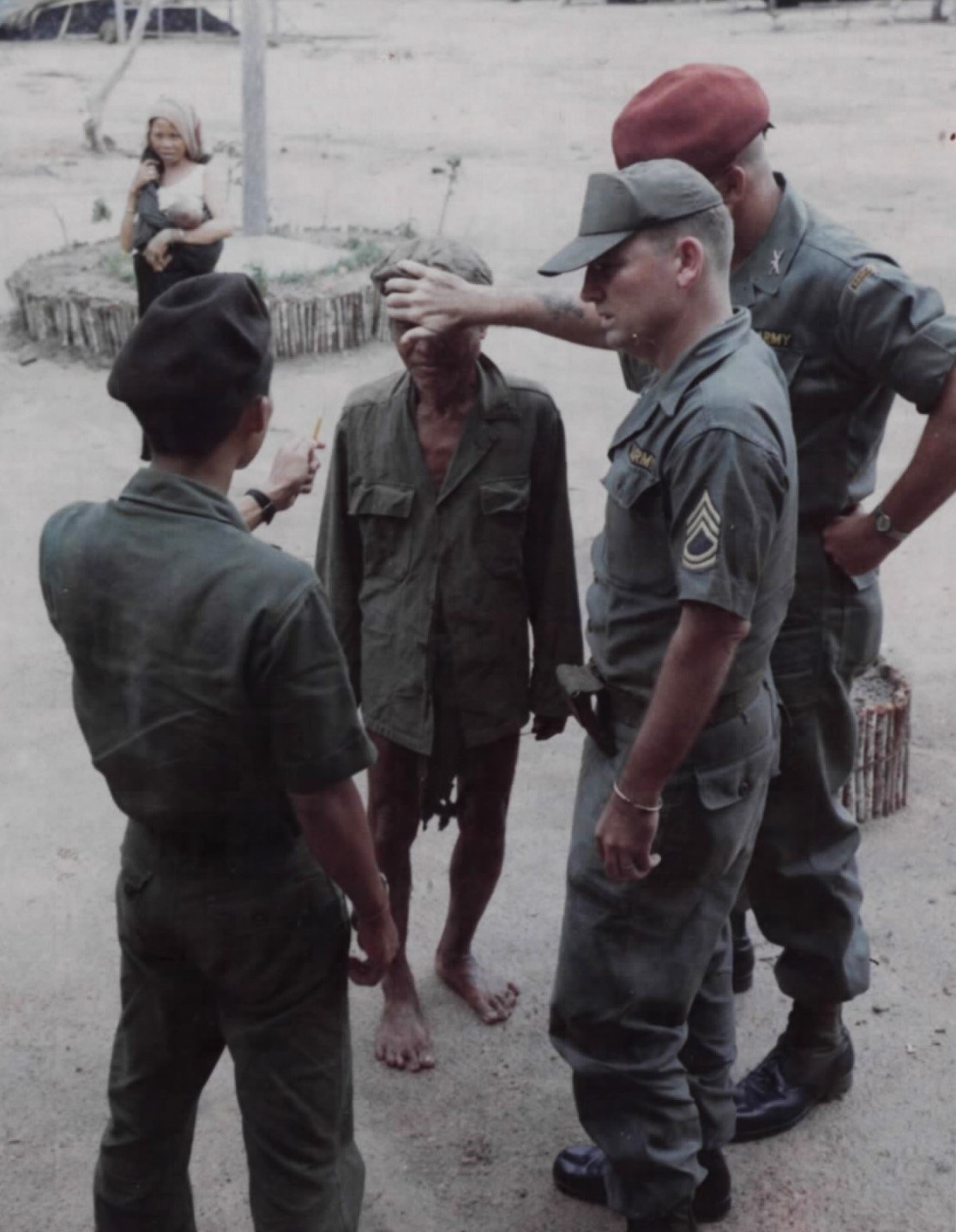 An American sergeant places his hand on the forehead of an elderly highland man, while other soldiers stand around them