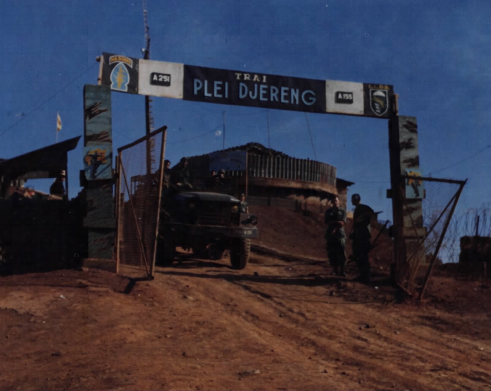 A timber gate with the sign Plei Djereng over a dirt road into a camp