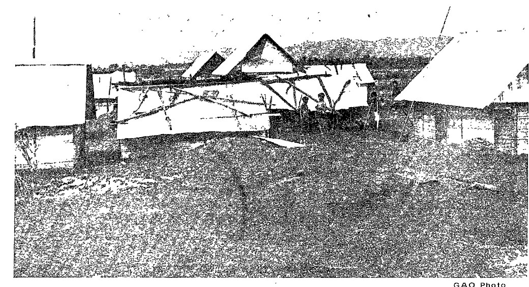 Grainy photograph of rough shelters of boards and tin among bare ground