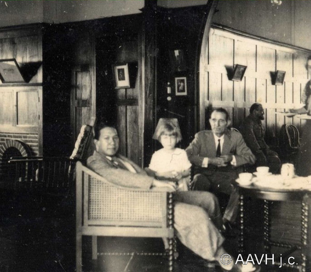 A group of men in white suits and an emperor on the veranda of a plantation house