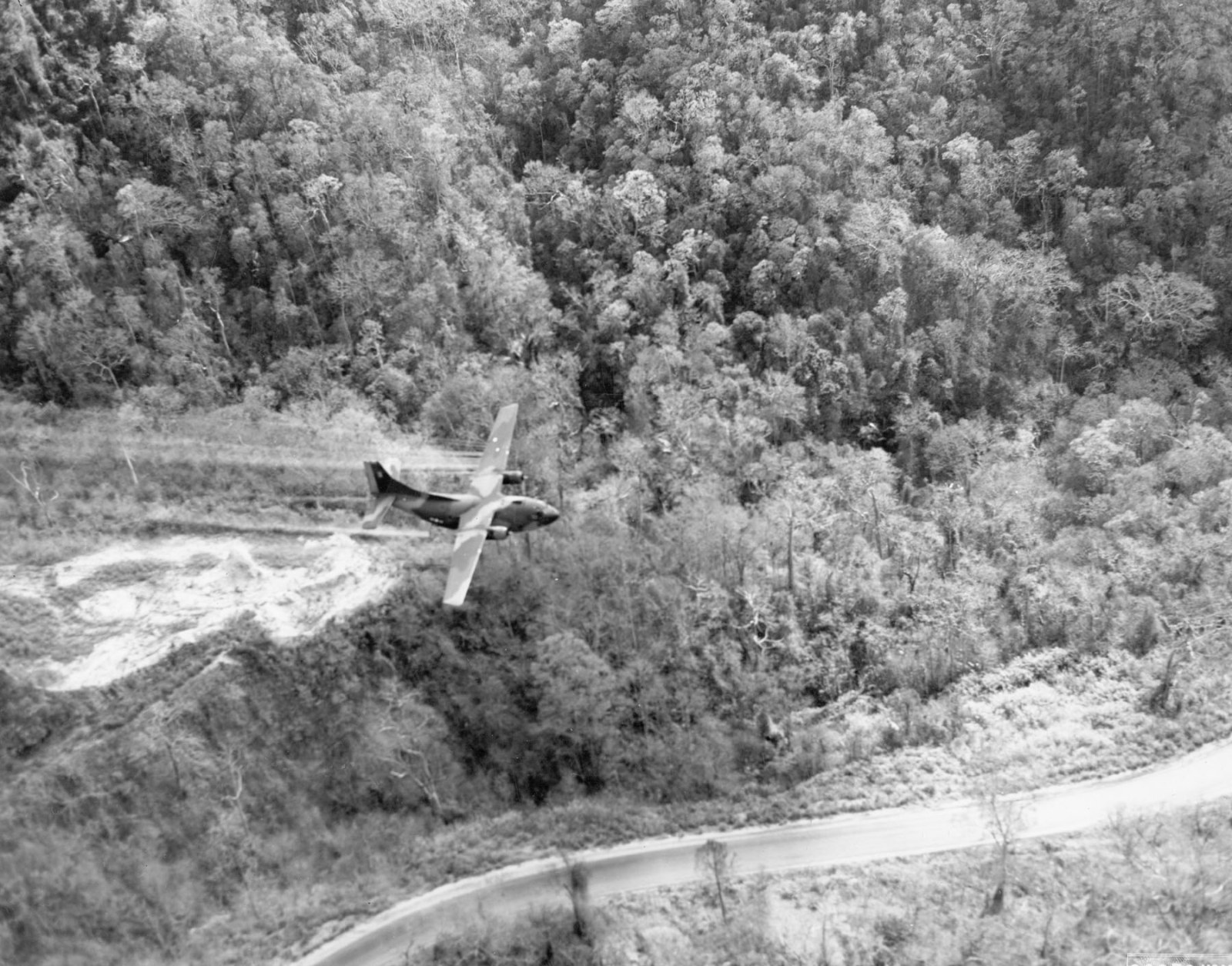 An aircraft flying low over a road through dense forest, spraying