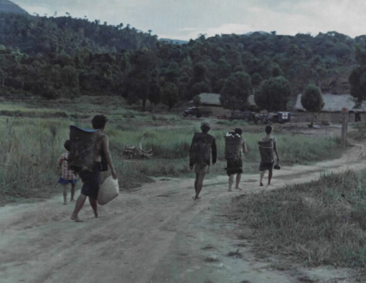 Highland villagers carrying baskets walk along a dirt road toward a relocated village