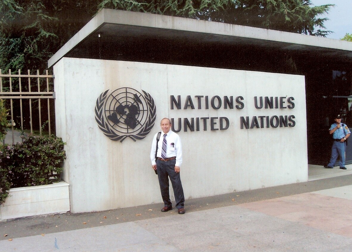 A man in a white shirt and tie stands in front of a wall marked Nations Unies, United Nations