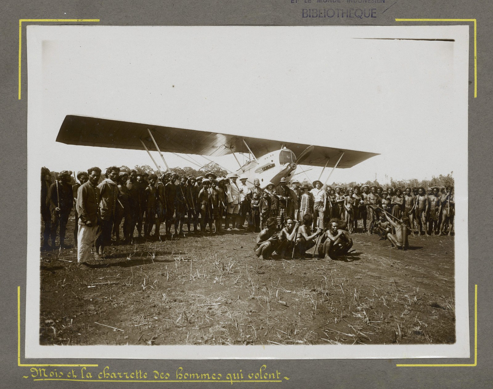 A group of highland men and French officers standing on an airstrip in front of a biplane