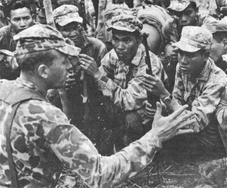 A Special Forces sergeant talks with a group of highland strike force soldiers crowded close around him