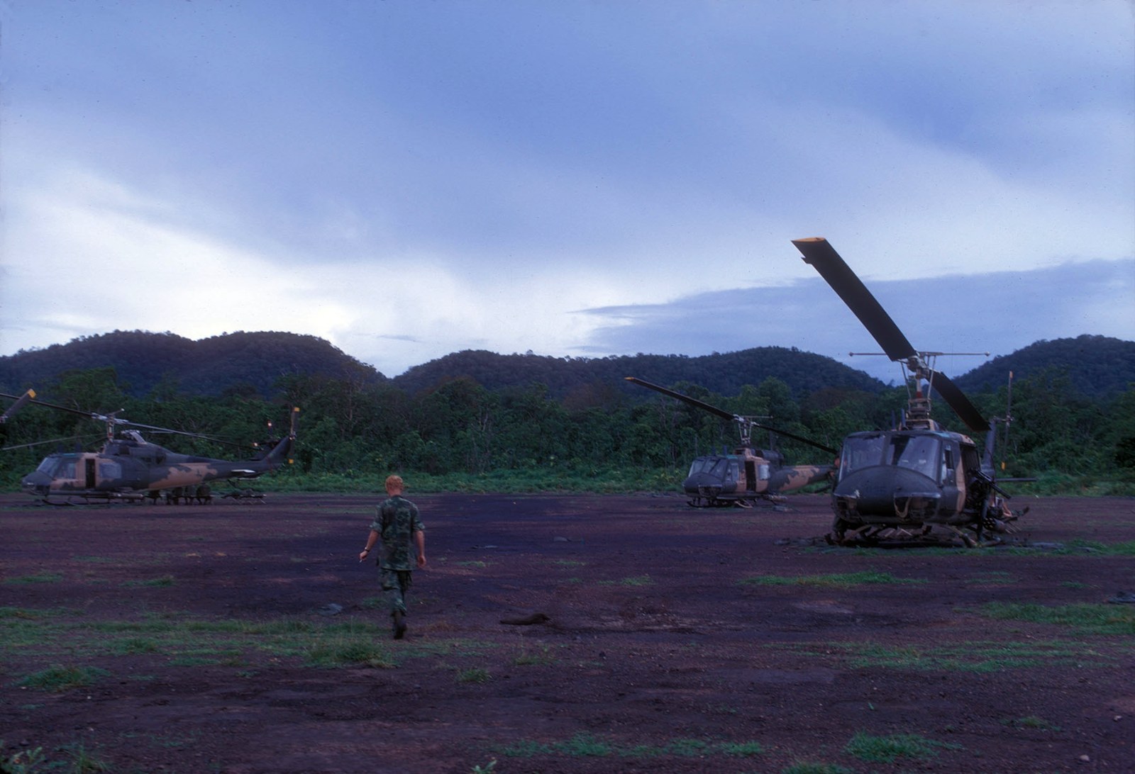 Two military helicopters on a dirt strip with a flat plain and hills behind