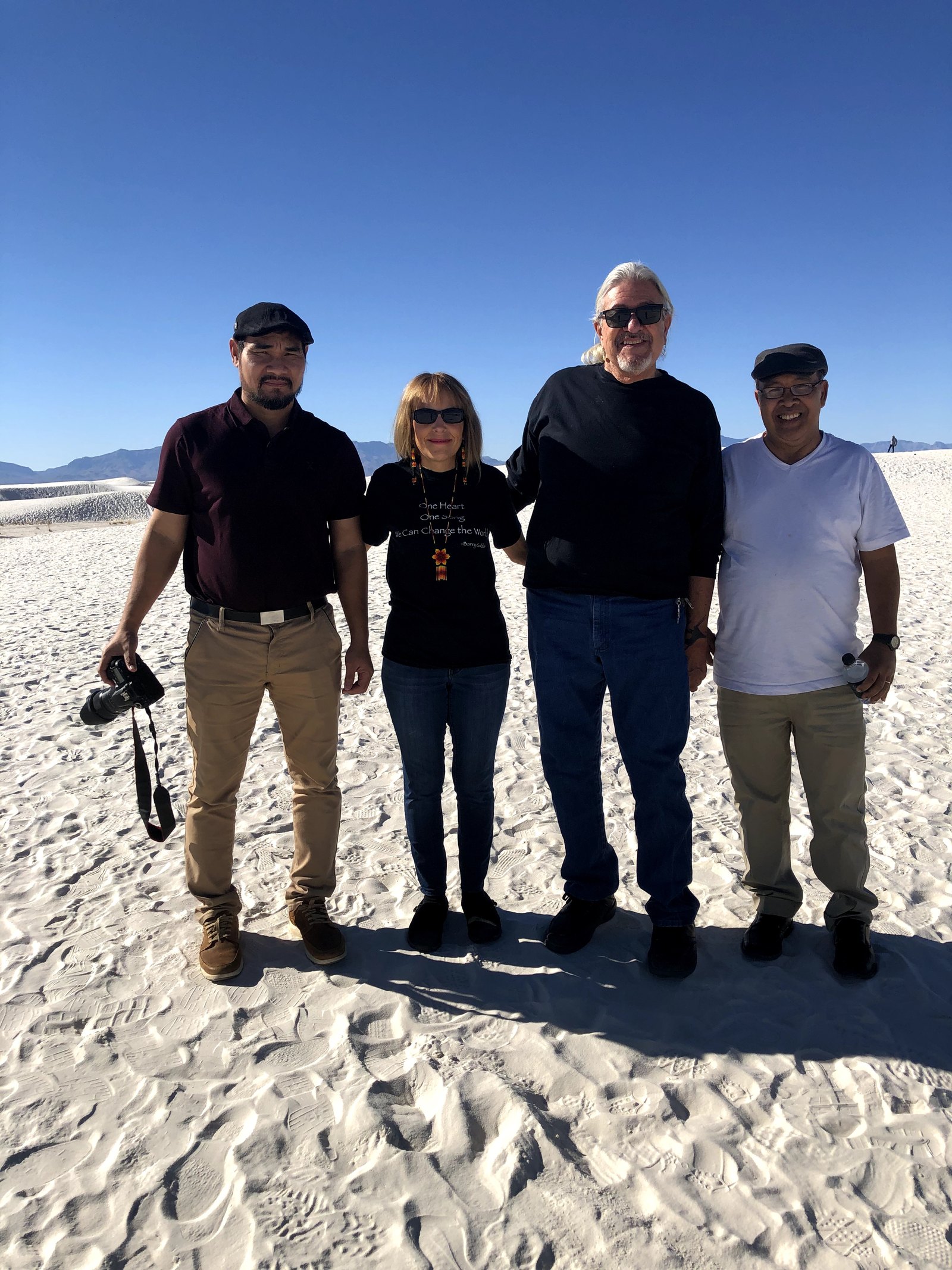 Four people standing together on the white gypsum dunes at White Sands under a clear blue sky