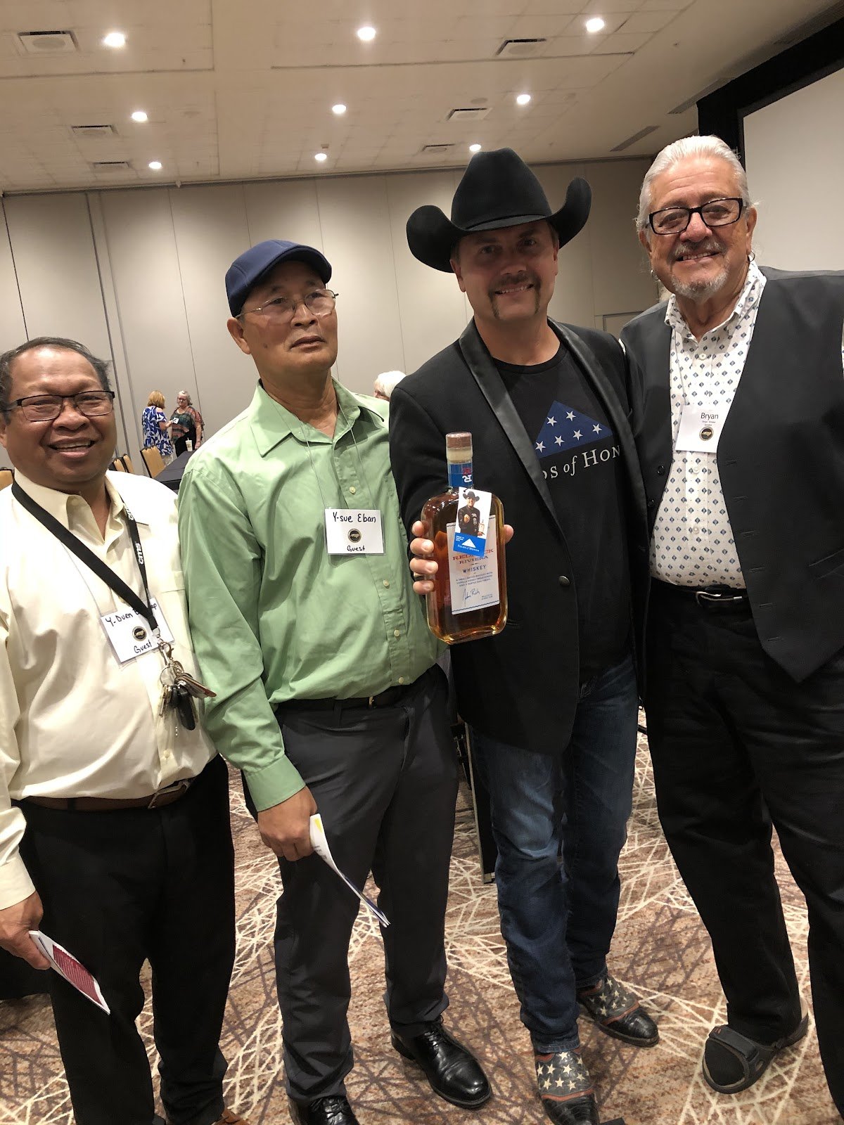 Four people standing together in the conference room, one holding a commemorative bottle