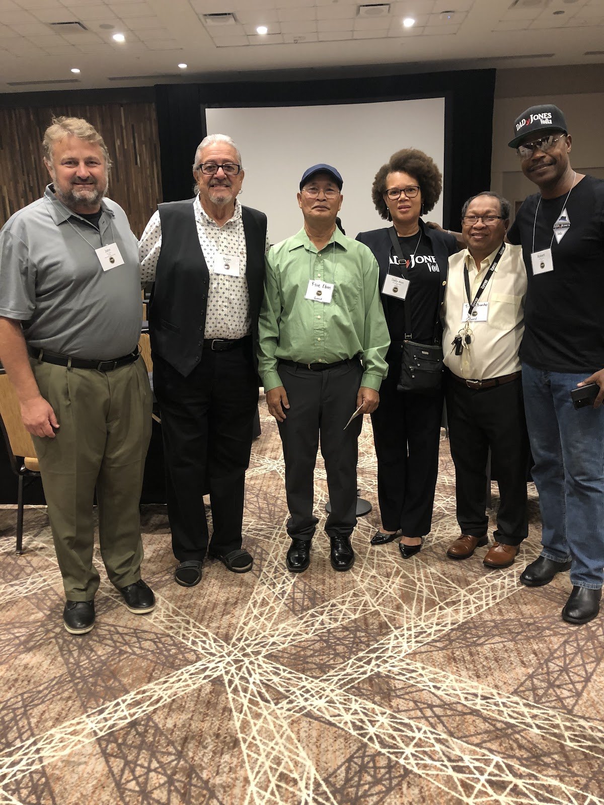 Six people standing together in a conference room, two of them Dega delegates wearing guest badges