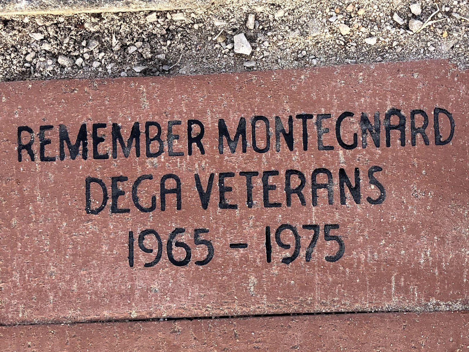 A red memorial brick set in the ground, inscribed REMEMBER MONTEGNARD DEGA VETERANS 1965 - 1975