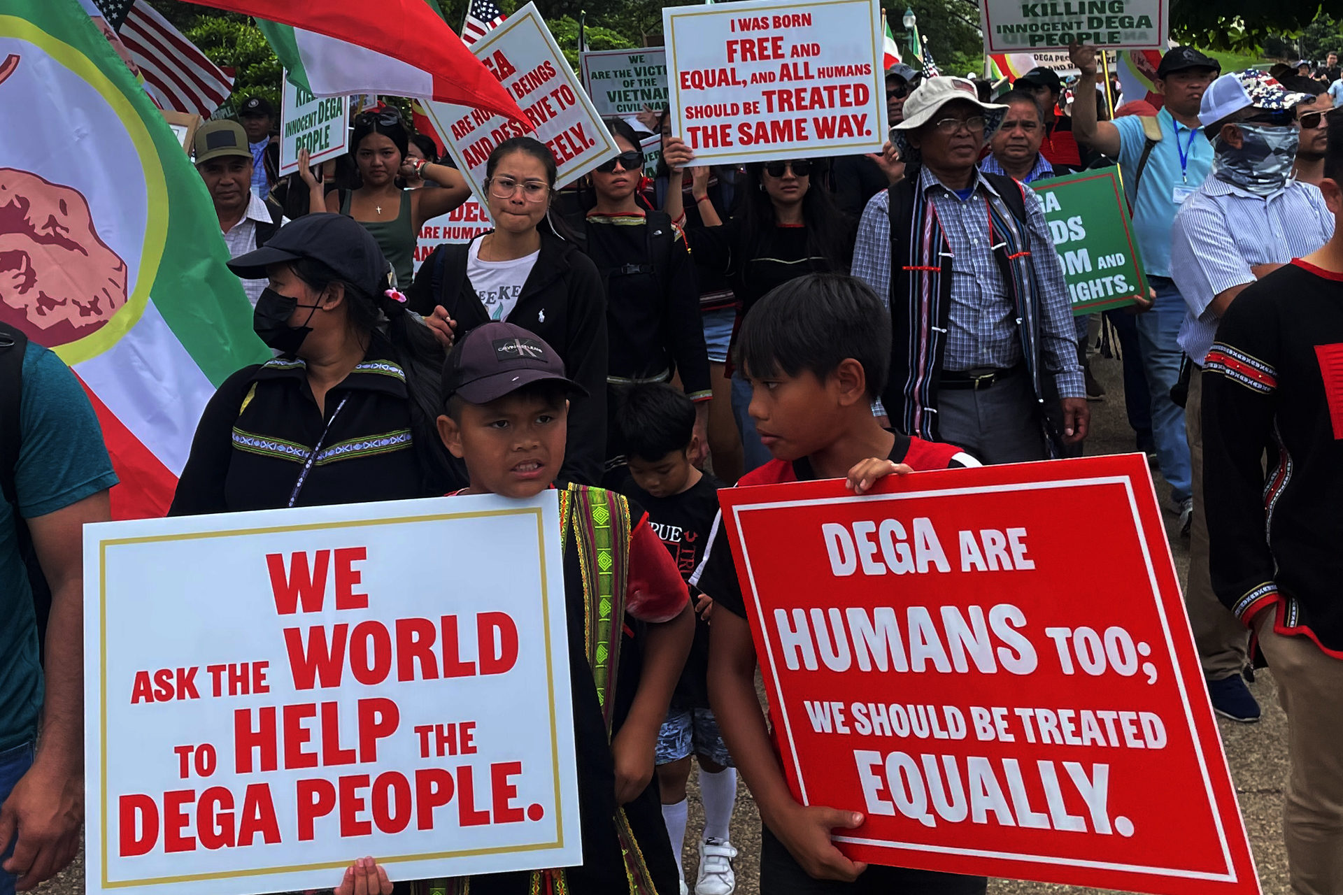 A crowd of marchers holding red and white signs reading Dega are humans too