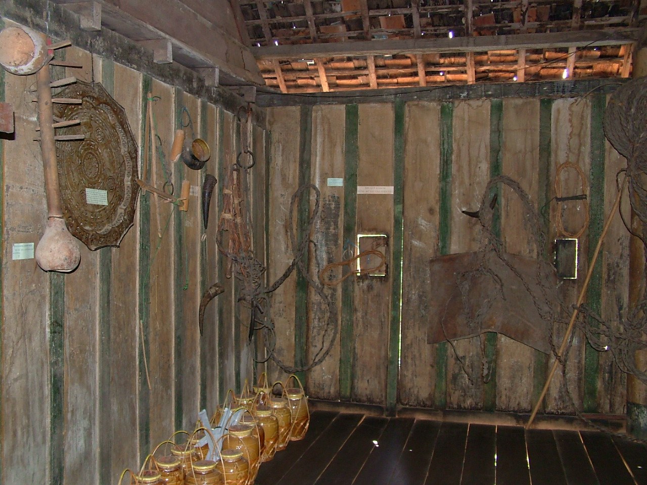 The inside of a wooden house with ropes, hides and hunting gear hung on the walls