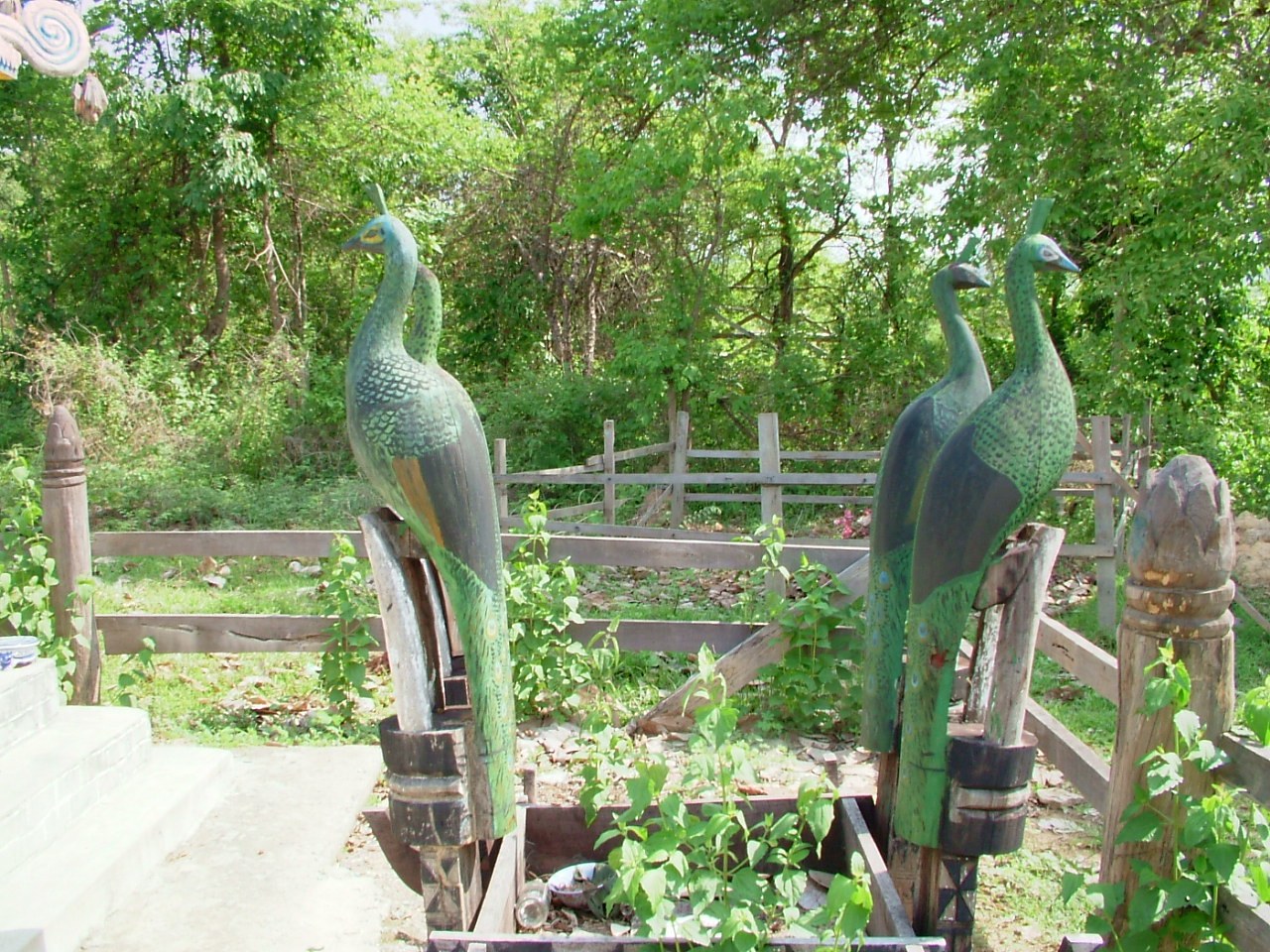 Two carved and painted wooden peacocks on posts at a grave