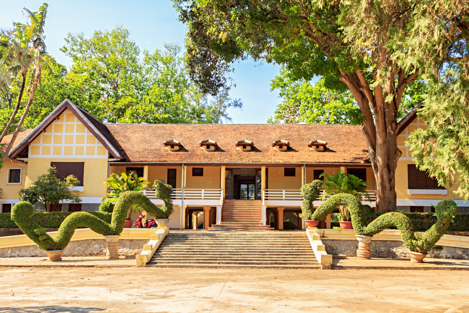 A colonial villa with a tiled roof among old trees