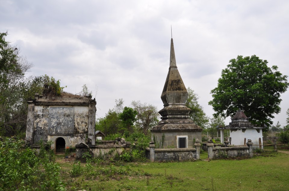 A tall tiered tomb tower and small shrines in a grassy cemetery