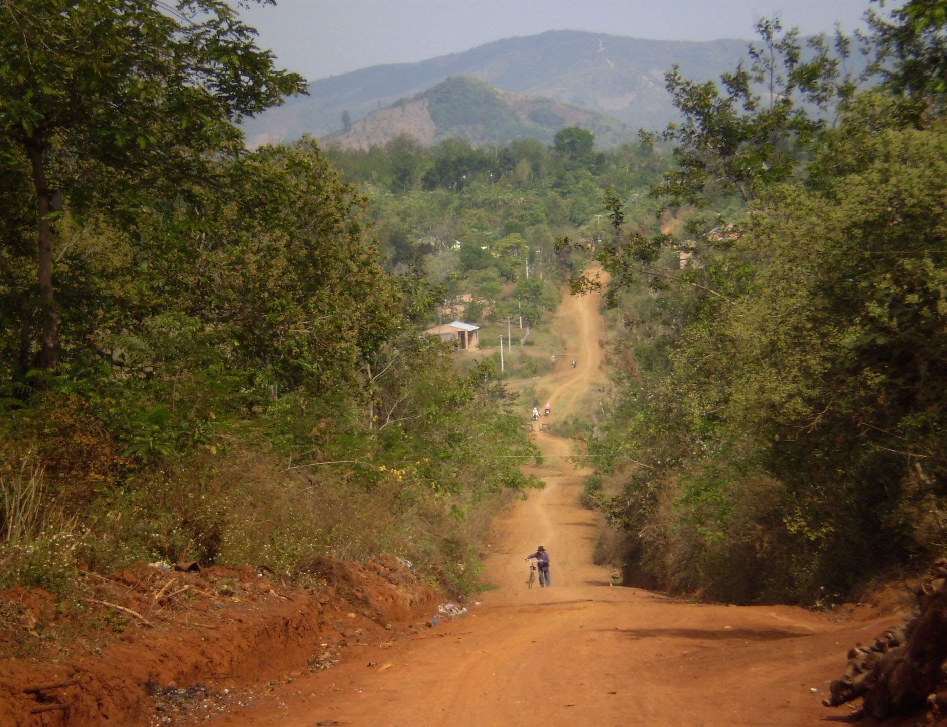 A red dirt road running through green scrub toward distant hills