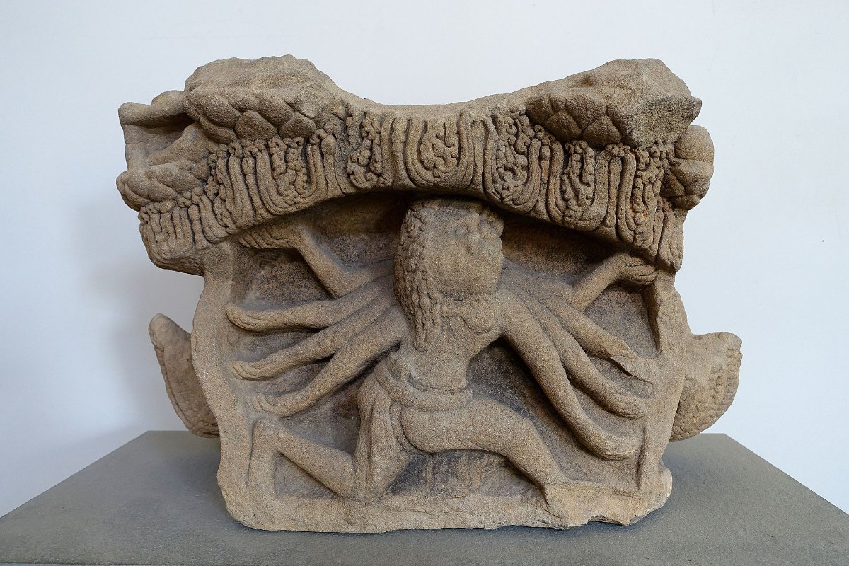 A carved sandstone altar pedestal from Dong Duong, with a many-armed figure and a frieze along its top, in a museum