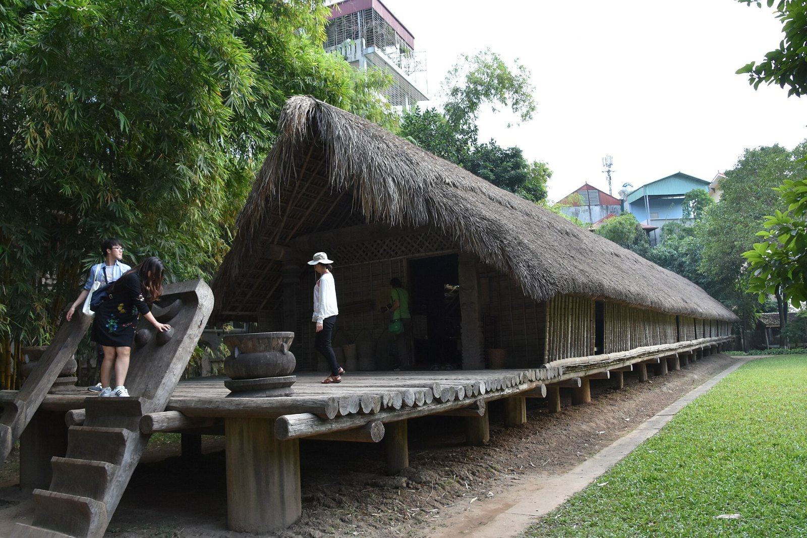 A long thatched house on piles standing in a museum garden