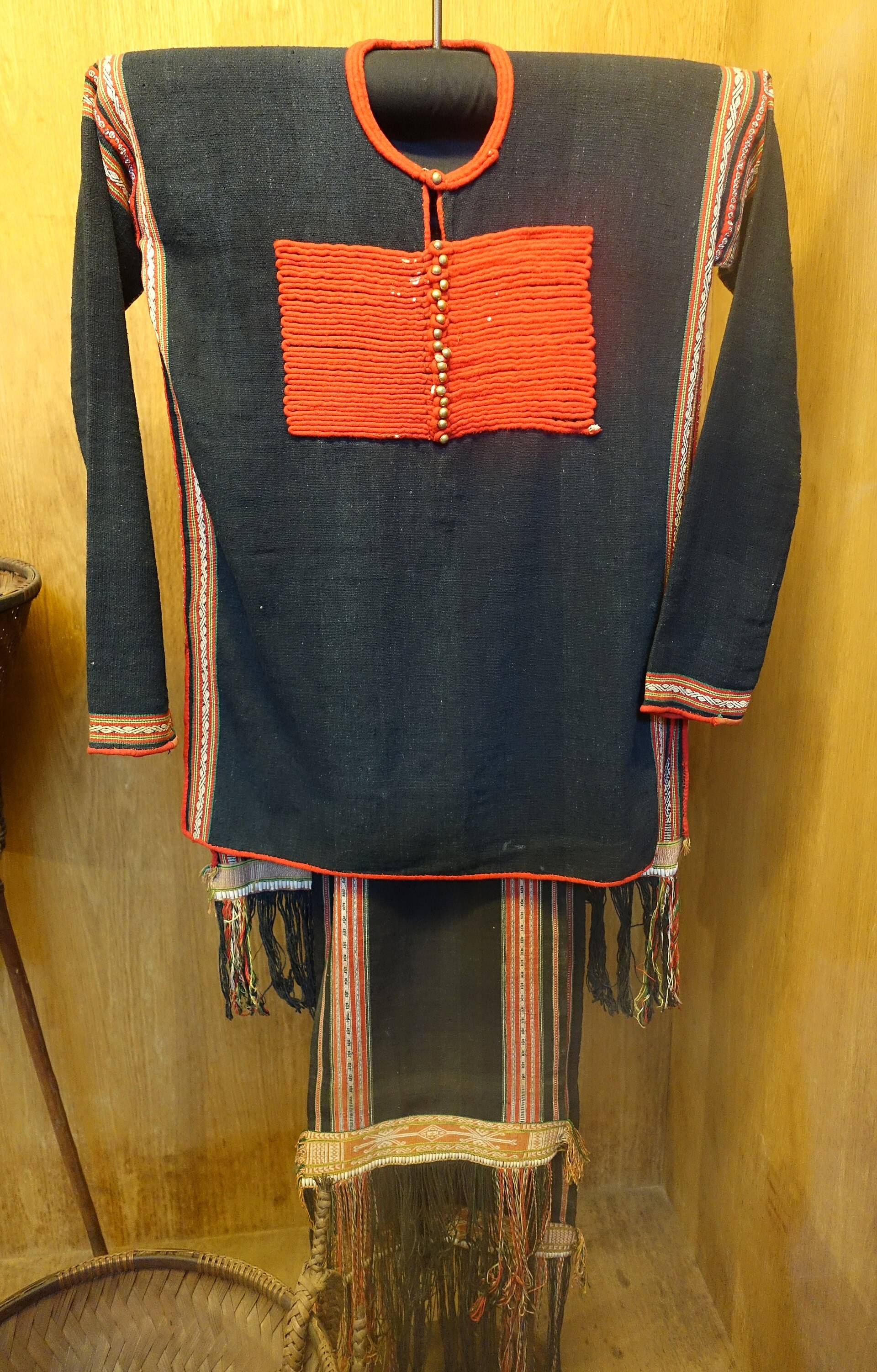 A dark indigo long-sleeved tunic with red bands and a long loincloth with patterned ends, on a museum figure