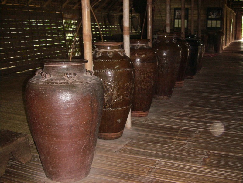 A row of large brown glazed jars standing along the floor of a wooden longhouse