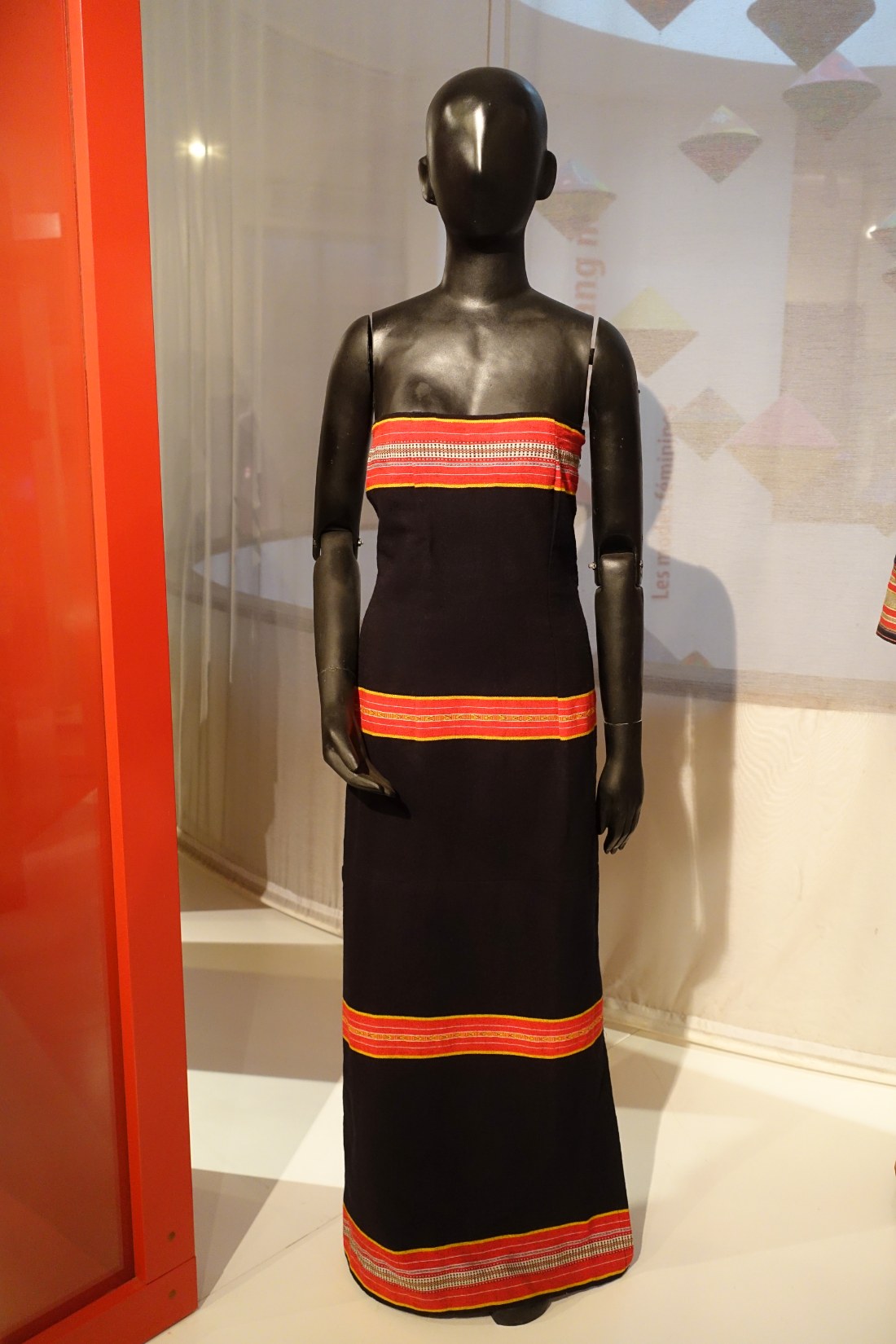 A dark woven costume with red bands on a museum figure