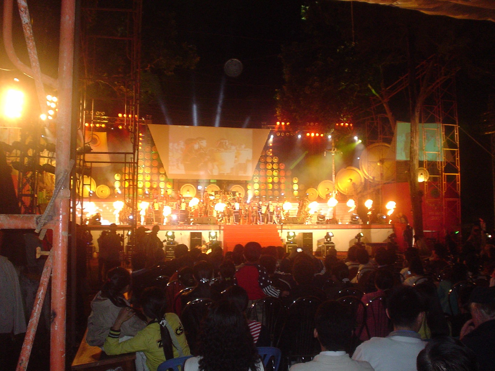 A crowd at night around performers at a gong festival, lit by stage lights