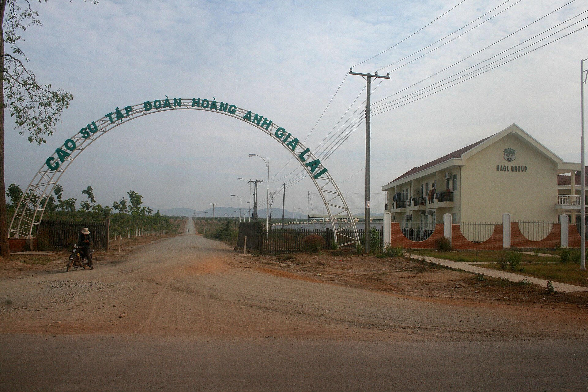 A white arched gate over a red dirt road reading Cao su Tập đoàn Hoàng Anh Gia Lai