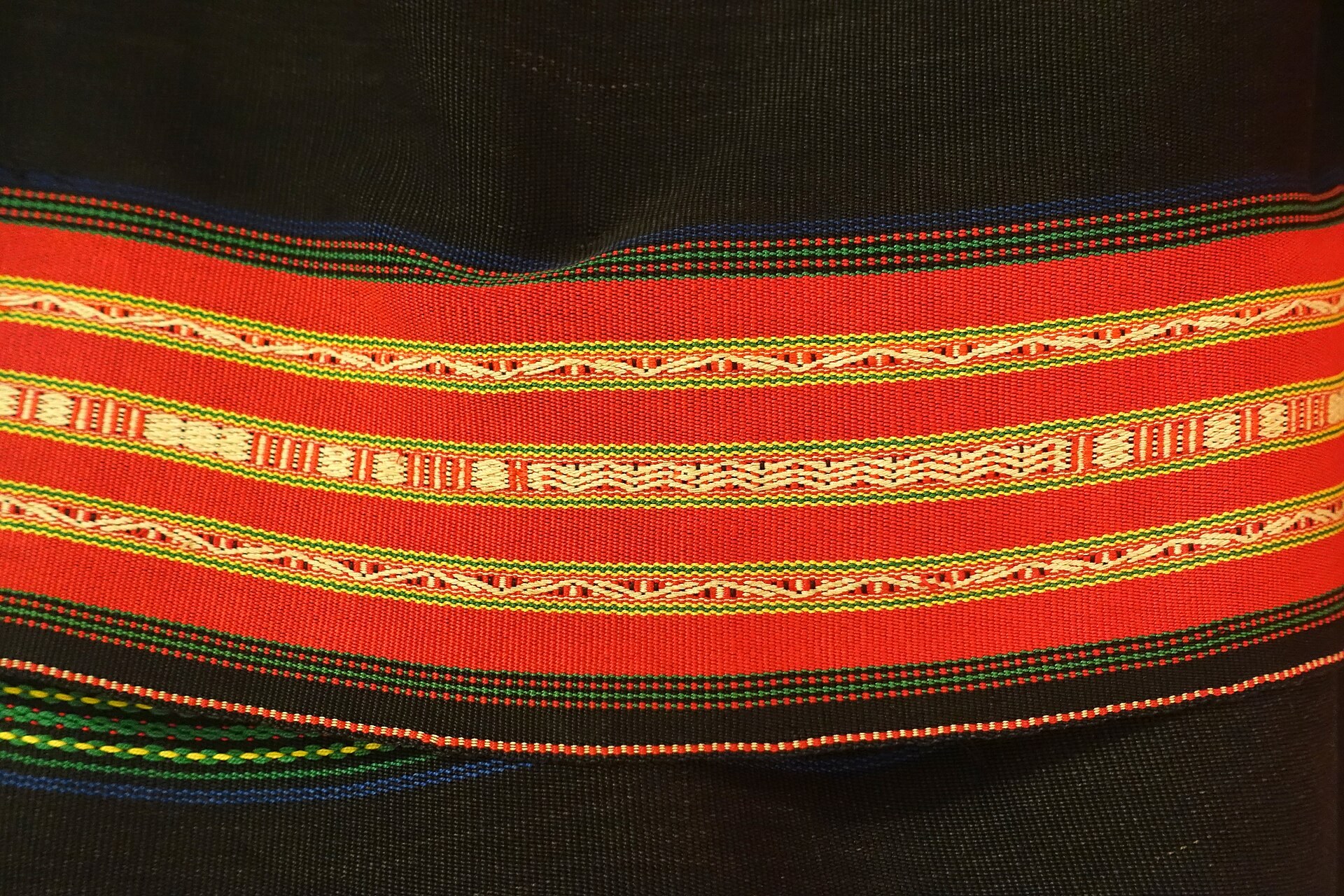 Close view of Jarai weaving: fine bands of red, white and yellow diamonds and lines on an indigo ground