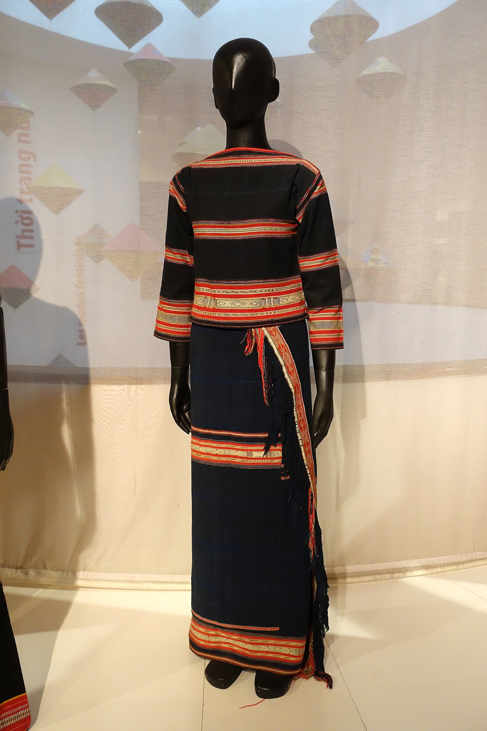 A Jarai woman’s dark skirt and blouse with narrow bands of red, yellow and white, on a museum figure
