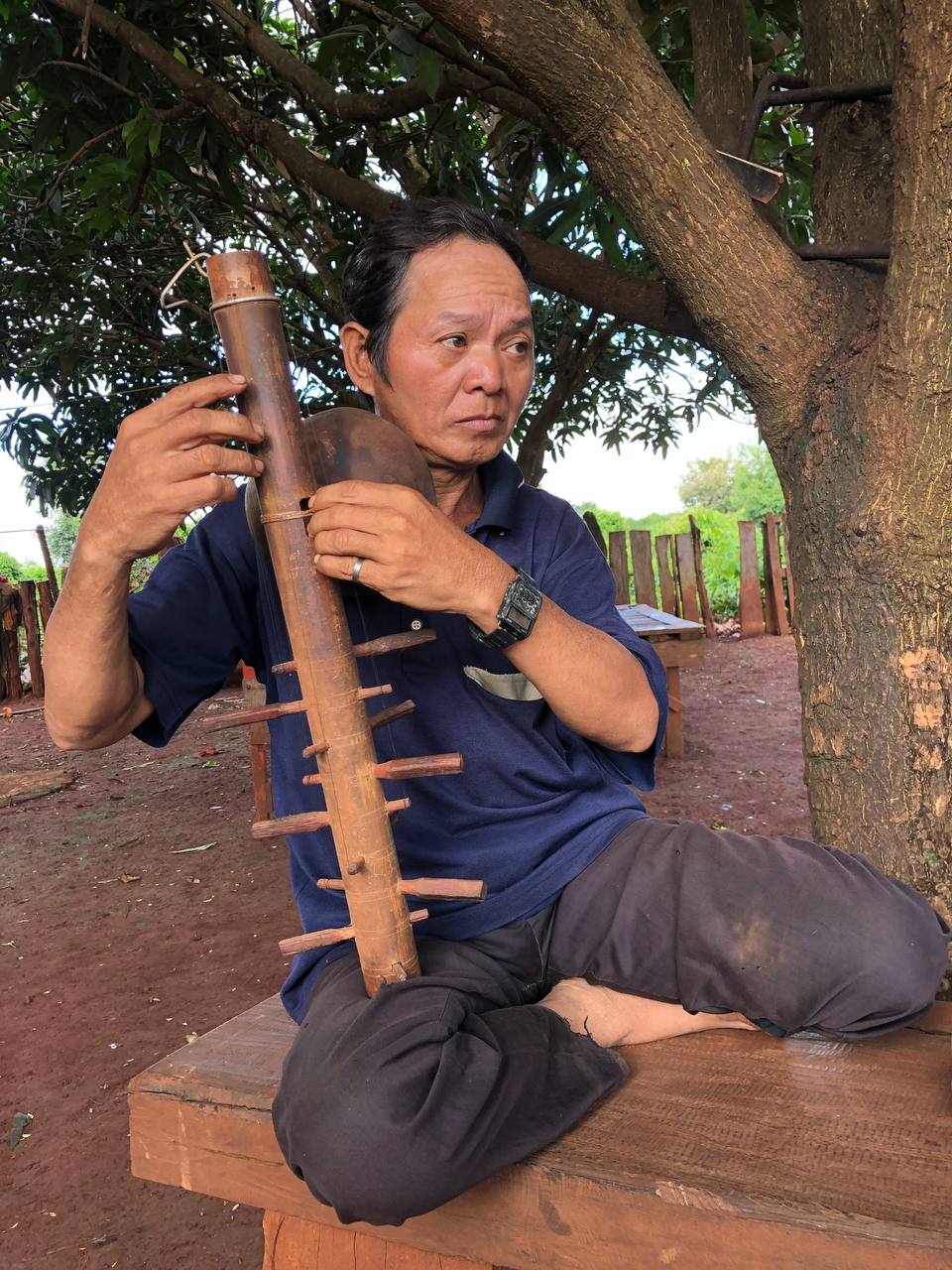 A Jarai man seated under a tree playing a long-necked string instrument