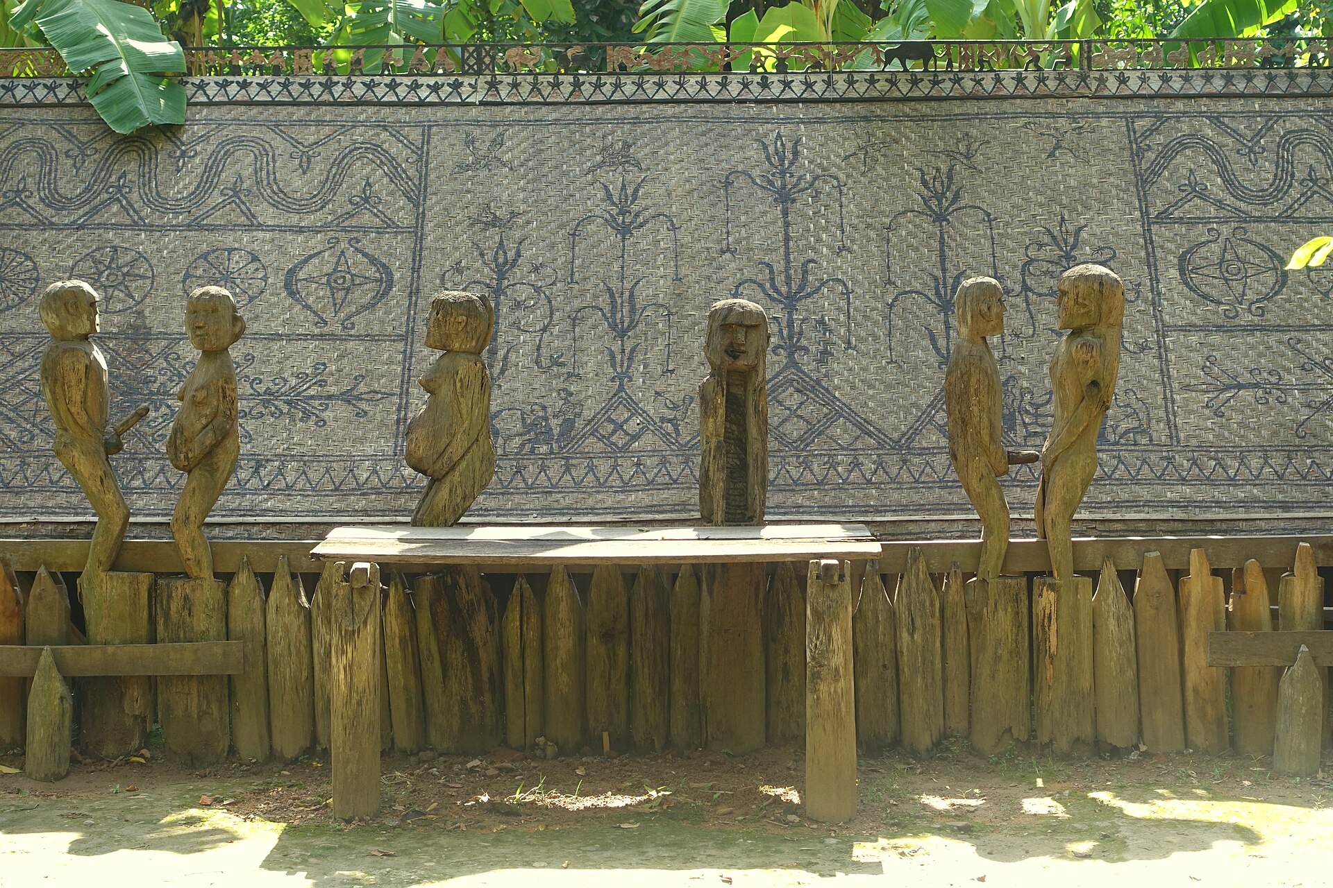 A Jarai tomb house with carved wooden figures in front of a decorated fence