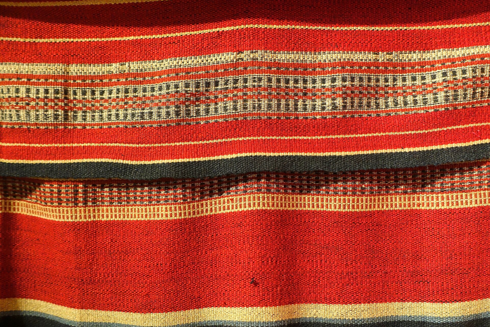 Detail of a red woven cloth with bands of pale patterning
